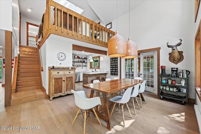 dining area featuring stairs, high vaulted ceiling, light wood finished floors, and french doors