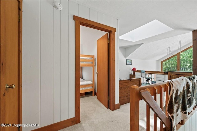 hall with a skylight, wooden walls, carpet flooring, and a textured ceiling