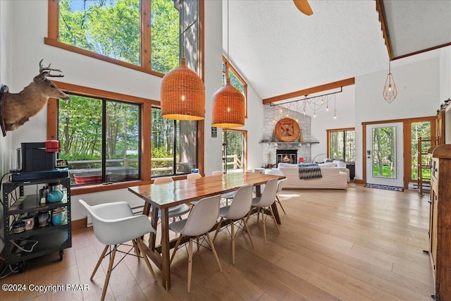 dining area with a textured ceiling, high vaulted ceiling, a stone fireplace, ceiling fan, and hardwood / wood-style flooring