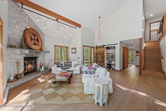 living room with a fireplace, wood-type flooring, a barn door, high vaulted ceiling, and stairs