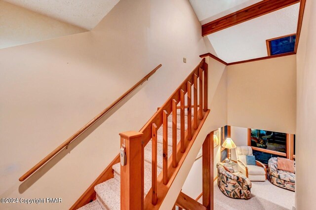 stairway with vaulted ceiling with beams, carpet, and baseboards