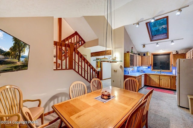 dining space featuring stairway, baseboards, rail lighting, lofted ceiling, and light colored carpet