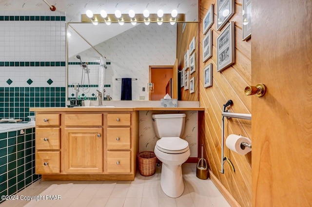 bathroom featuring toilet, tile patterned flooring, wallpapered walls, tiled shower, and vanity