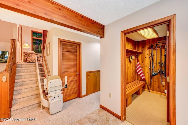 interior space with stairway, wooden walls, baseboards, a textured ceiling, and light colored carpet