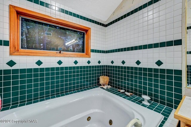 bathroom featuring a jetted tub, tile walls, and vaulted ceiling