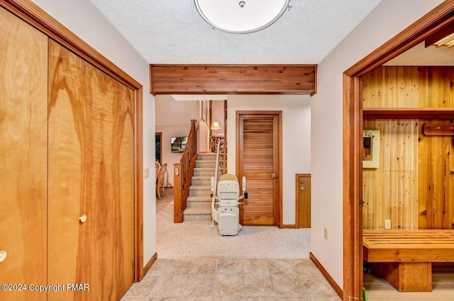 hallway featuring beam ceiling, a textured ceiling, stairway, baseboards, and light colored carpet