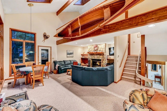 carpeted living room featuring baseboards, high vaulted ceiling, a stone fireplace, stairs, and beamed ceiling