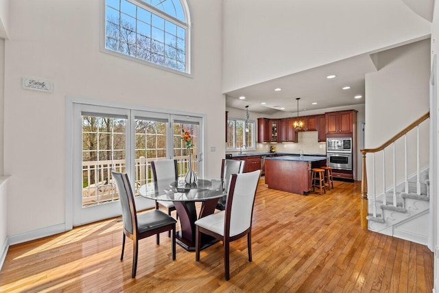 dining area featuring light wood-style floors, stairway, recessed lighting, and a towering ceiling