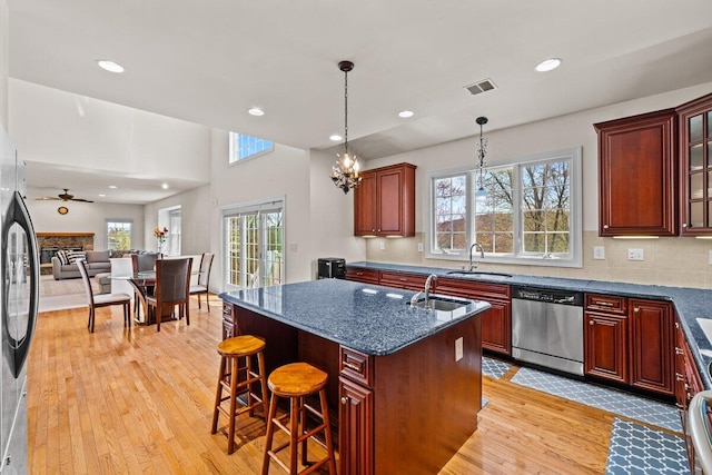 kitchen with light wood-style floors, a sink, a kitchen island with sink, and dishwasher