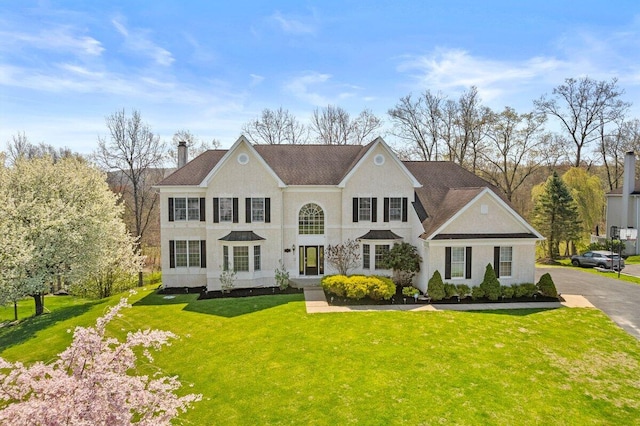 view of front facade featuring a front lawn, stucco siding, and a chimney