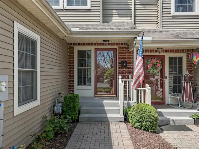 doorway to property with brick siding and a shingled roof