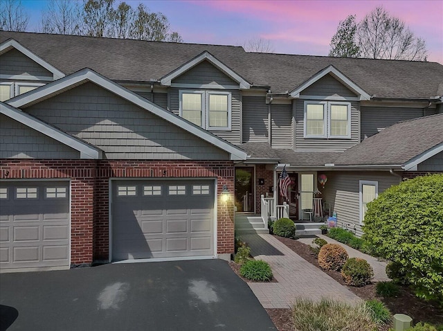 view of front of home with a shingled roof, an attached garage, driveway, and brick siding