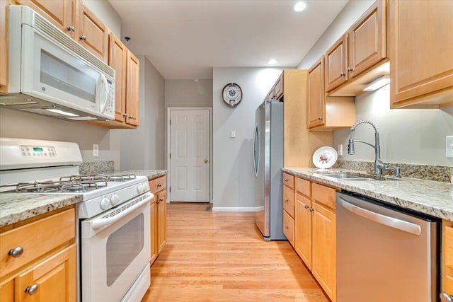 kitchen featuring appliances with stainless steel finishes, a sink, light wood finished floors, and light stone counters