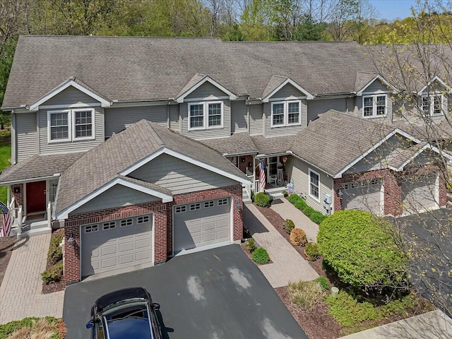view of front facade with brick siding, a shingled roof, an attached garage, driveway, and a porch