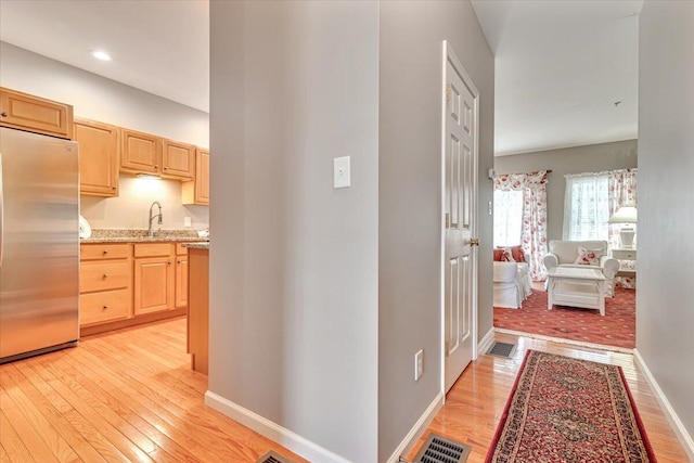 hallway featuring light wood-style floors, baseboards, and visible vents