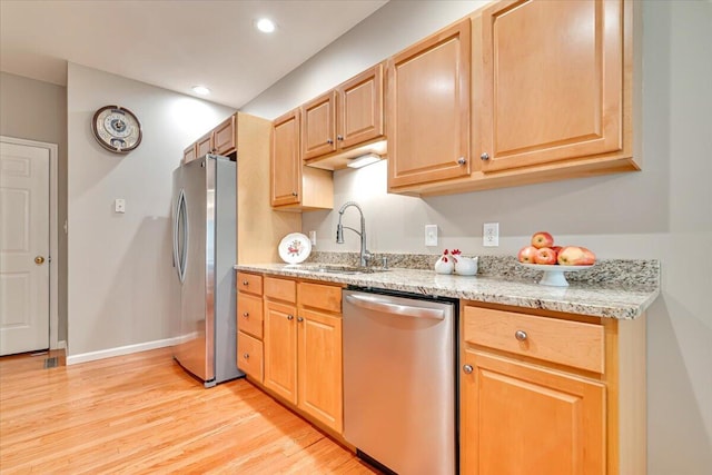 kitchen with recessed lighting, light stone counters, a sink, light wood-style flooring, and stainless steel appliances