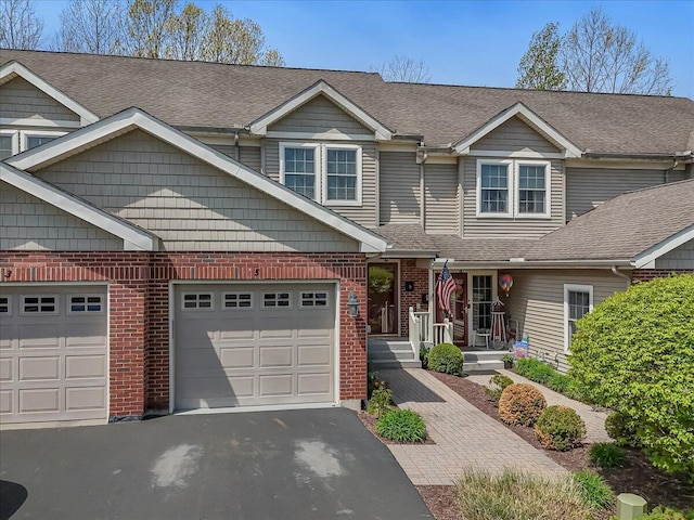 view of front of property featuring an attached garage, roof with shingles, driveway, and brick siding