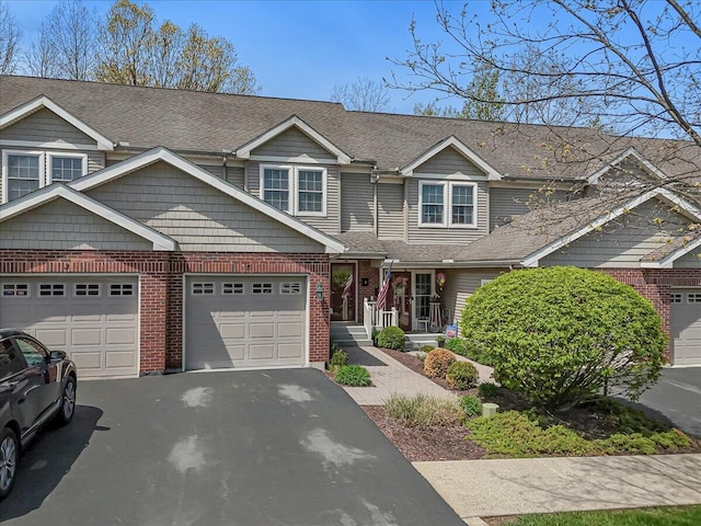 townhome / multi-family property with brick siding, a shingled roof, an attached garage, and driveway