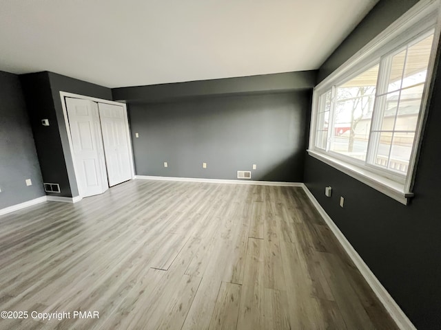 unfurnished bedroom featuring light wood-style floors, a closet, visible vents, and baseboards