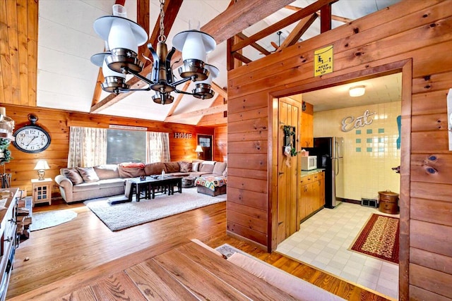 living room featuring light wood finished floors, wooden walls, beamed ceiling, an inviting chandelier, and high vaulted ceiling