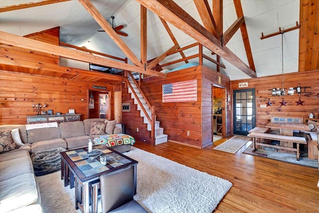 living area with beamed ceiling, wood finished floors, wooden walls, ceiling fan, and stairs