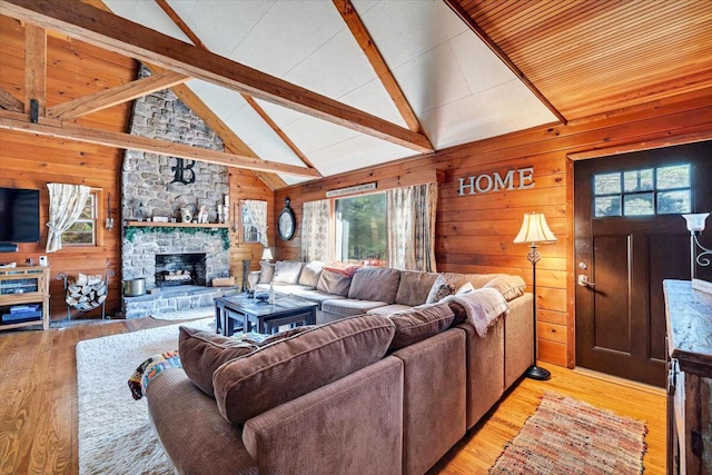 living area featuring a stone fireplace, light wood-type flooring, wooden walls, and beamed ceiling