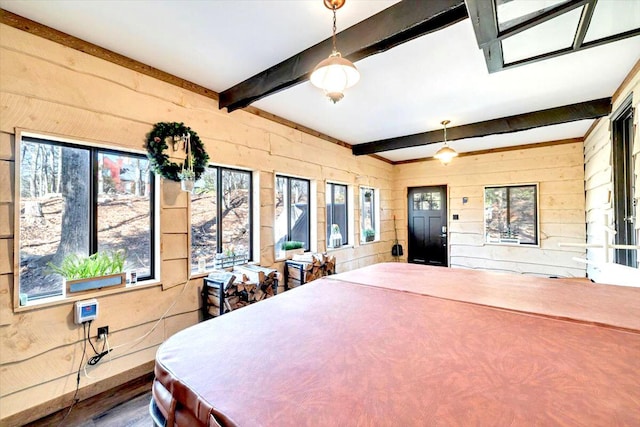 bedroom with beam ceiling, wooden walls, and wood finished floors