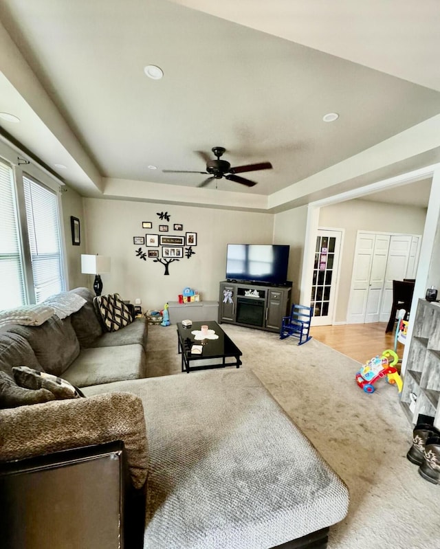 carpeted living area featuring a raised ceiling and a ceiling fan