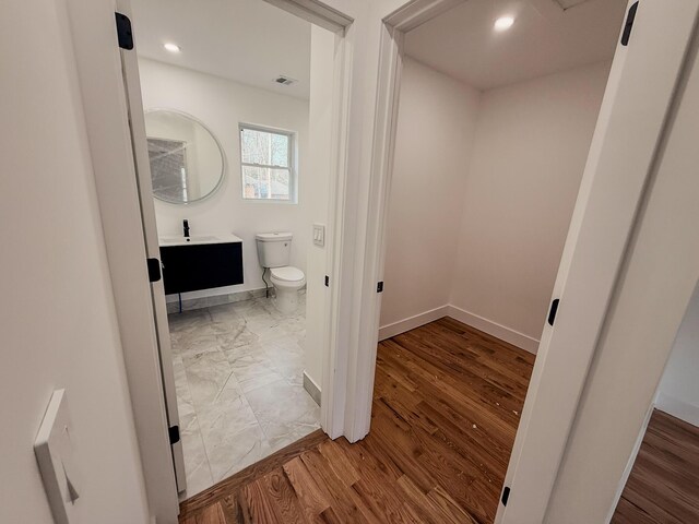 kitchen with stainless steel microwave, light stone counters, light wood-type flooring, white cabinetry, and a sink