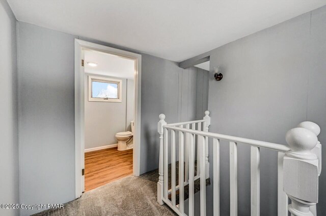 hallway with an upstairs landing, baseboards, and carpet floors