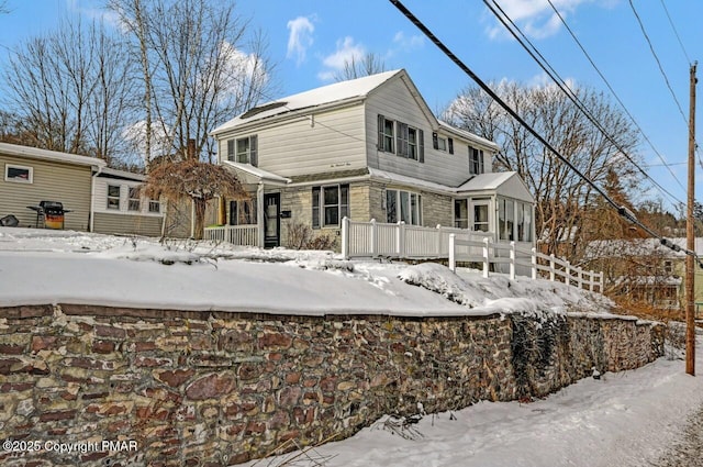 snow covered rear of property featuring stone siding