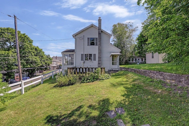 back of house with a lawn, a chimney, a sunroom, and fence