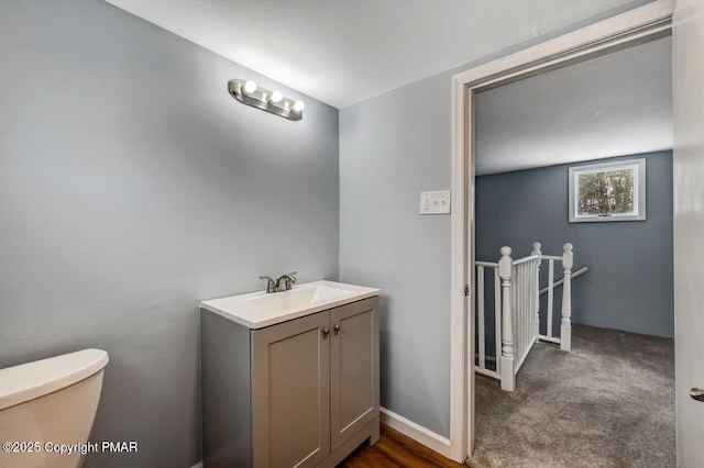 half bath with baseboards, toilet, and vanity