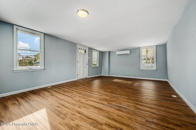 unfurnished room featuring an AC wall unit, plenty of natural light, wood finished floors, and baseboards