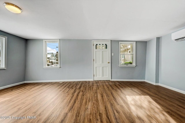 spare room with an AC wall unit, baseboards, and wood finished floors