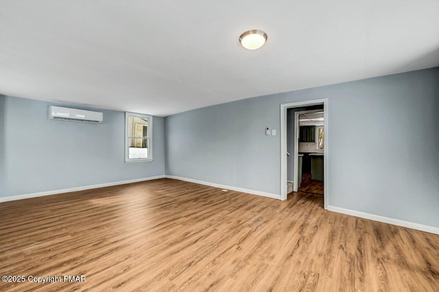 spare room with baseboards, a wall unit AC, and wood finished floors