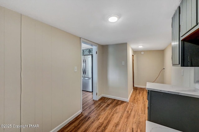 kitchen featuring baseboards, freestanding refrigerator, light wood-style floors, and light stone countertops