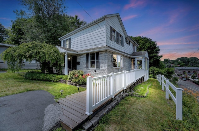 property exterior at dusk with a lawn and stone siding