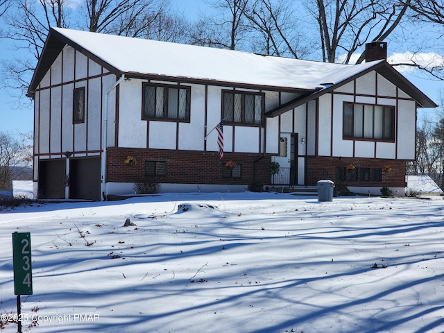 tudor house featuring stucco siding, brick siding, a garage, and a chimney