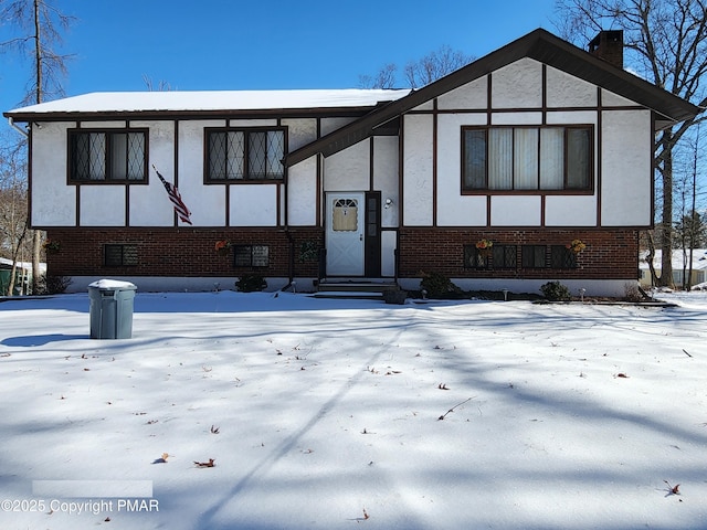 english style home featuring entry steps, brick siding, a chimney, and stucco siding