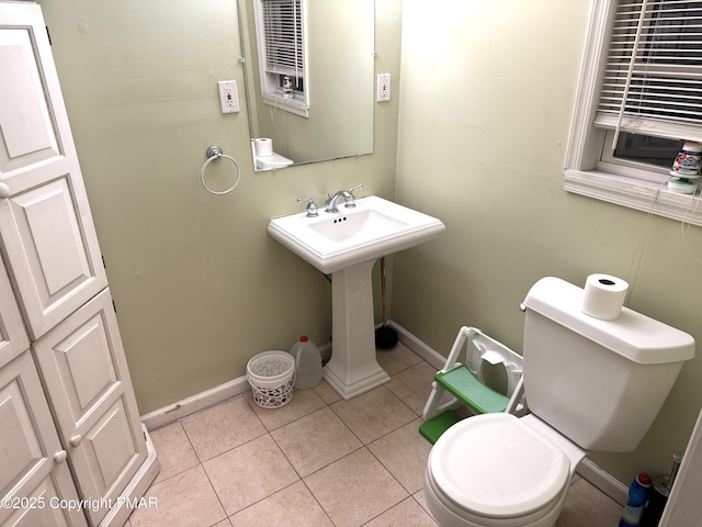 half bath featuring baseboards, a sink, toilet, and tile patterned floors