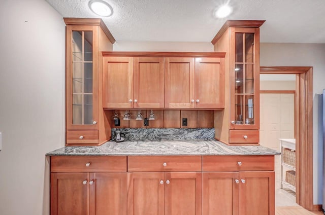 3110 Tall Timber Lake Rd, Pocono Pines, PA 18350 - kitchen with light stone counters, a textured ceiling, glass insert cabinets, and brown cabinetry