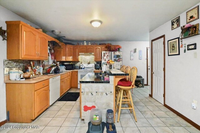 kitchen with white appliances, under cabinet range hood, light tile patterned floors, and a kitchen breakfast bar