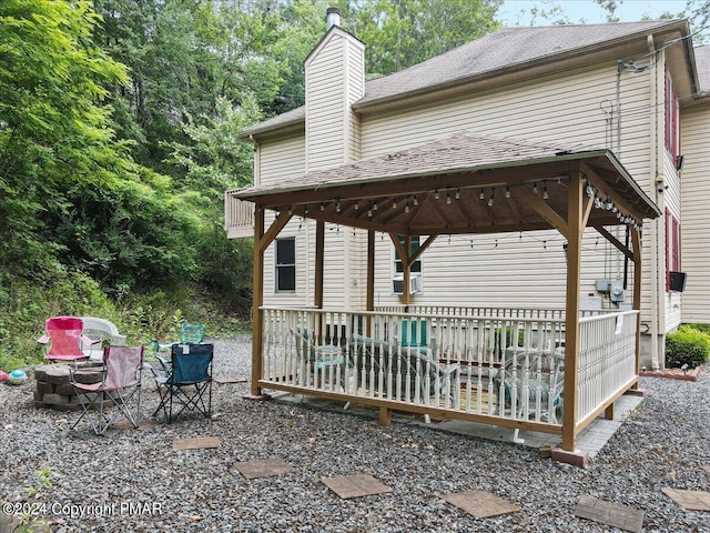 back of house with roof with shingles, a chimney, and a gazebo