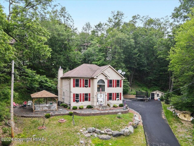 view of front of property with aphalt driveway, a gazebo, a front lawn, a chimney, and a view of trees