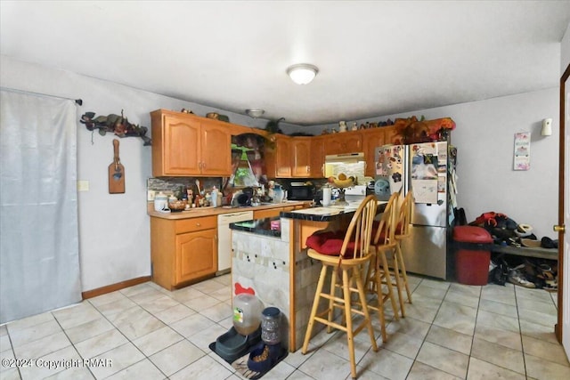 kitchen featuring light tile patterned flooring, a kitchen breakfast bar, dishwasher, and freestanding refrigerator