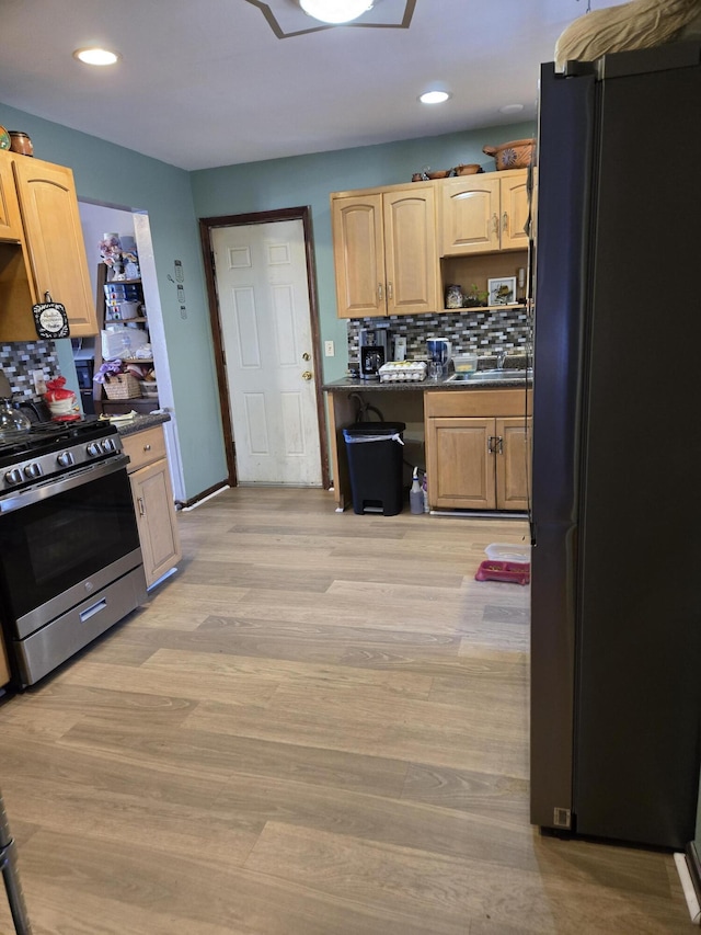 kitchen with light wood-style floors, backsplash, freestanding refrigerator, stainless steel gas stove, and dark countertops