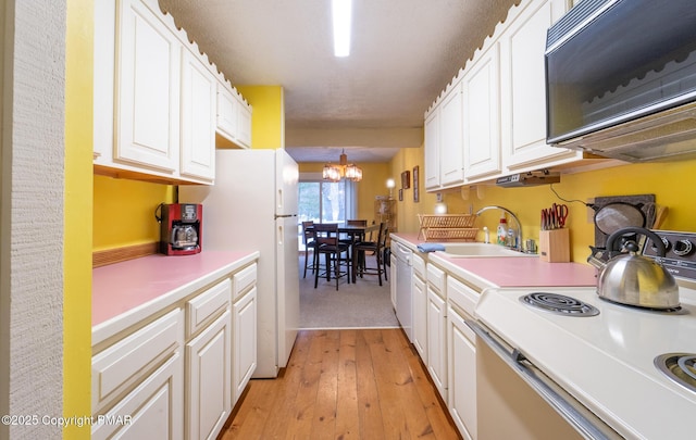 kitchen with a chandelier, white appliances, white cabinetry, light countertops, and light wood finished floors