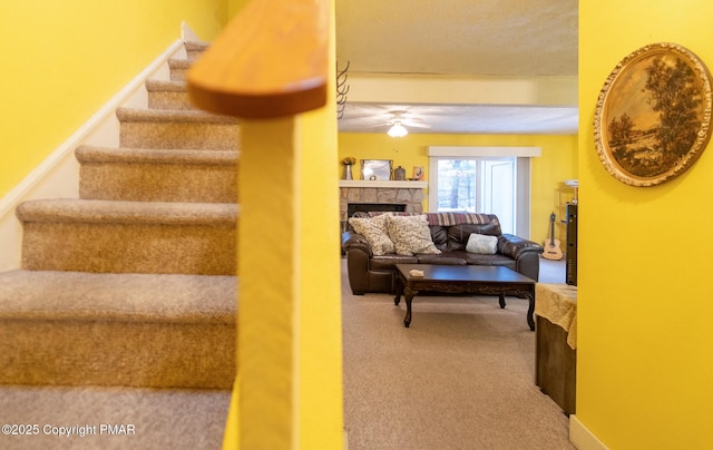 stairs with carpet, a ceiling fan, and a stone fireplace