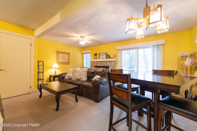 living area with a textured ceiling, carpet floors, ceiling fan with notable chandelier, and a tiled fireplace